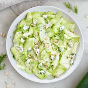 zucchini ribbons with nuts, cheese, herbs, and dressing on a plate