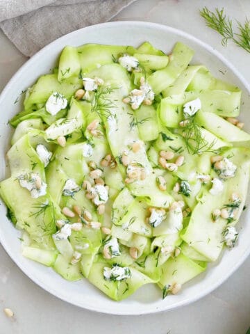 zucchini ribbons with nuts, cheese, herbs, and dressing on a plate