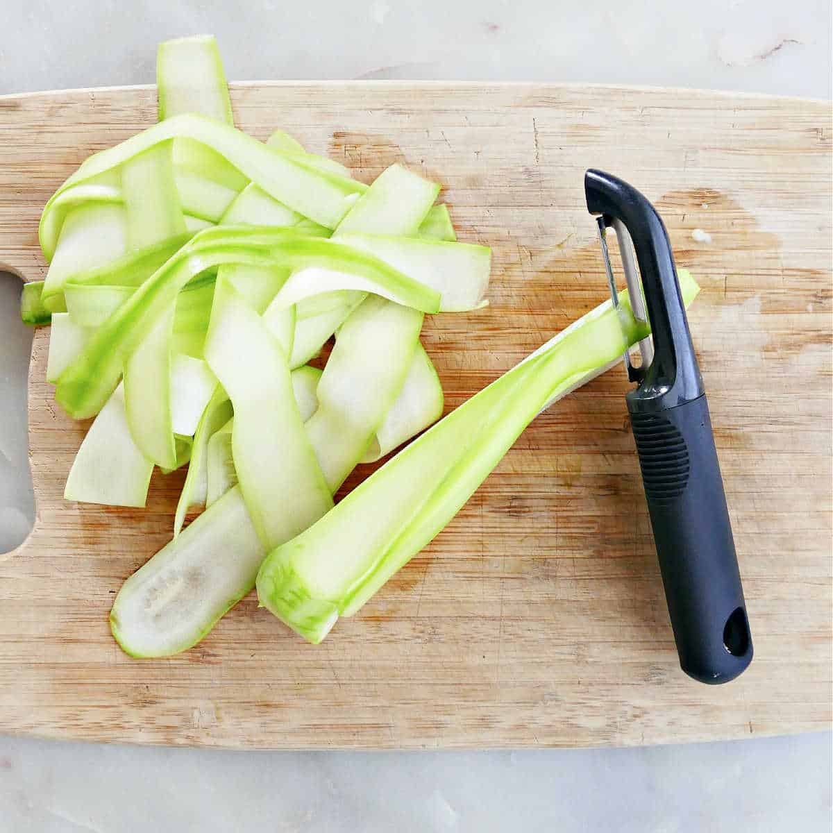 raw zucchini being shaved into ribbons on a cutting board