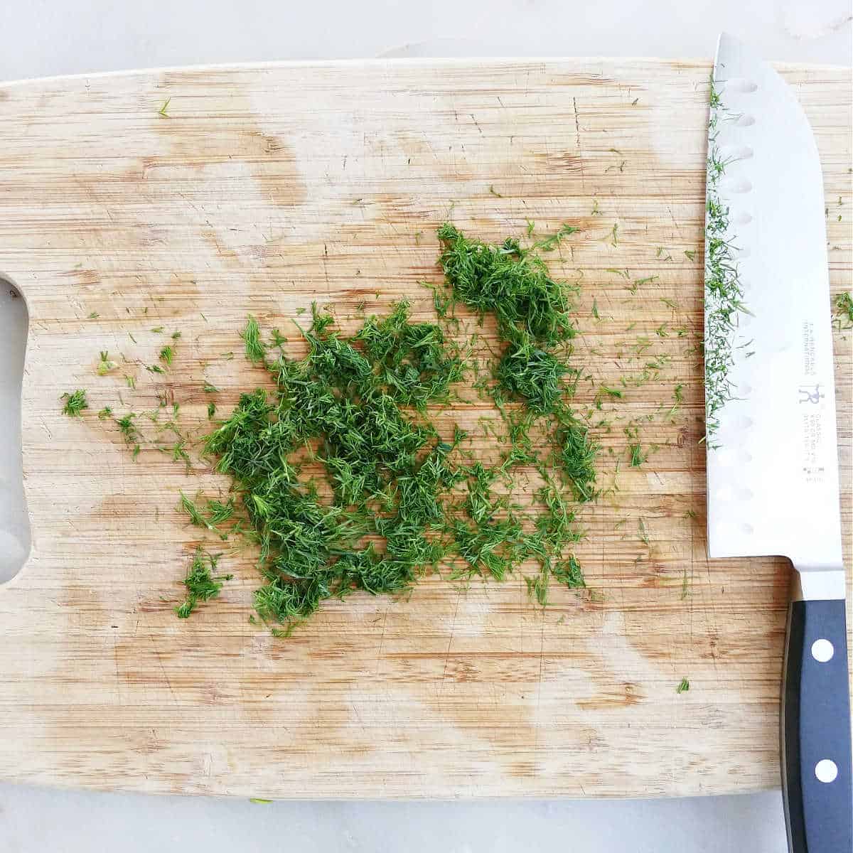chopped fresh dill on a cutting board next to a knife
