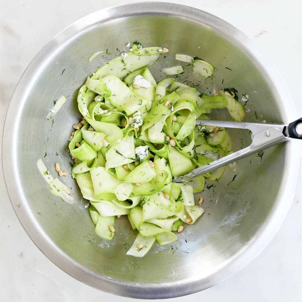zucchini ribbons salad being tossed in a bowl with tongs