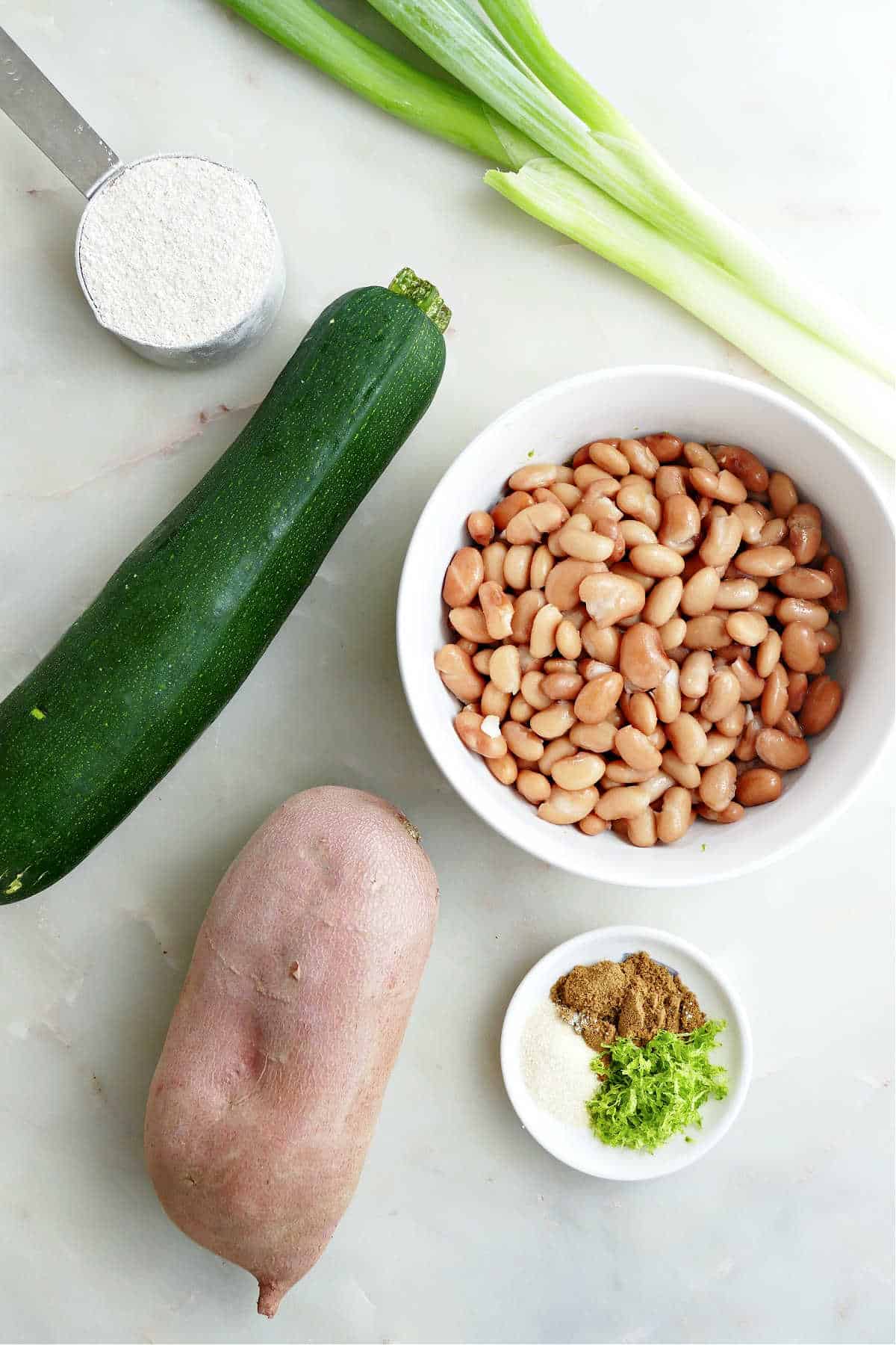 zucchini, flour, green onion, pinto beans, seasonings, and sweet potato on a counter