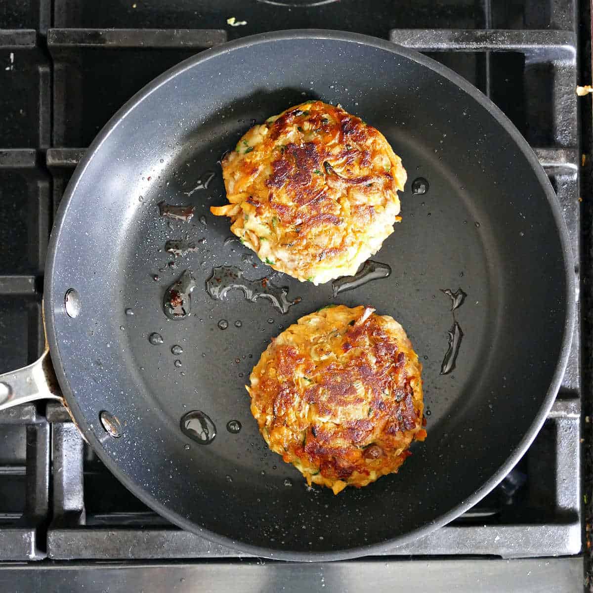 2 fritters cooking in oil in a skillet on the stove