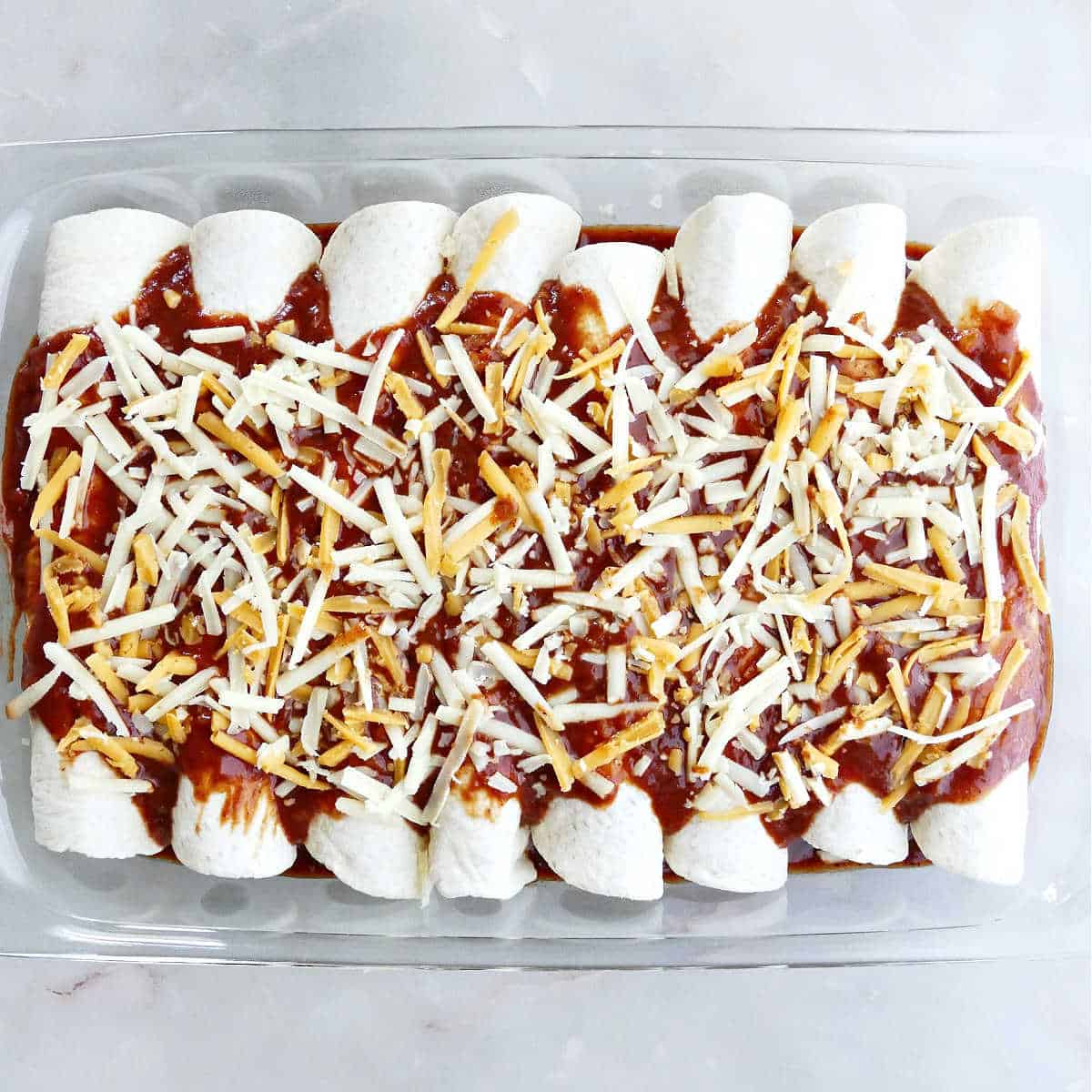 enchiladas covered with sauce and shredded cheese in a baking dish before being baked