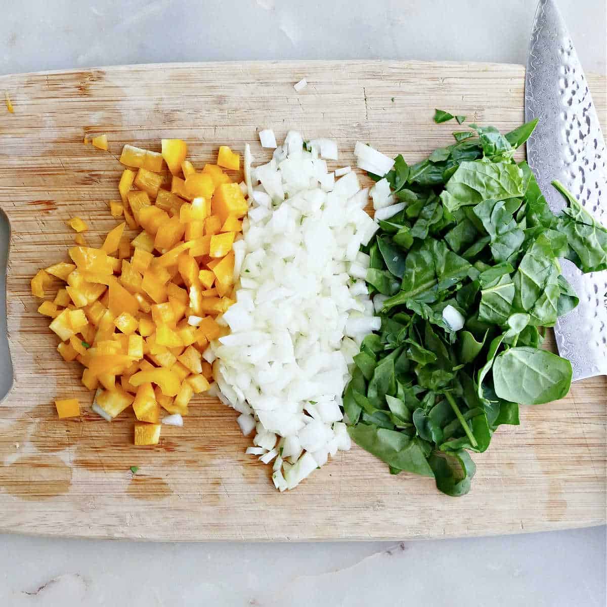 chopped peppers, onion, and spinach on a cutting board with a knife