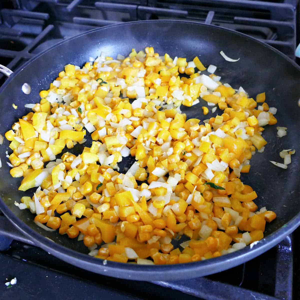 peppers, onions, and corn cooking in oil in a skillet on a stove