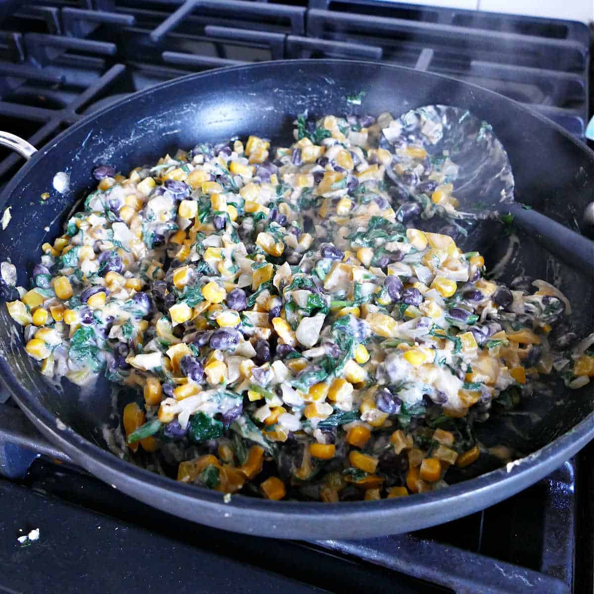 black bean and spinach enchilada filling cooking in a skillet on a stove