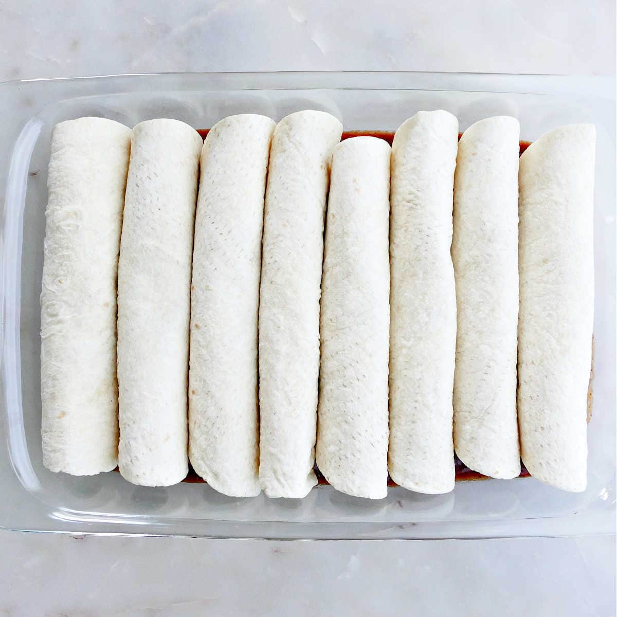 filled enchiladas rolled up and placed in a rectangular baking dish