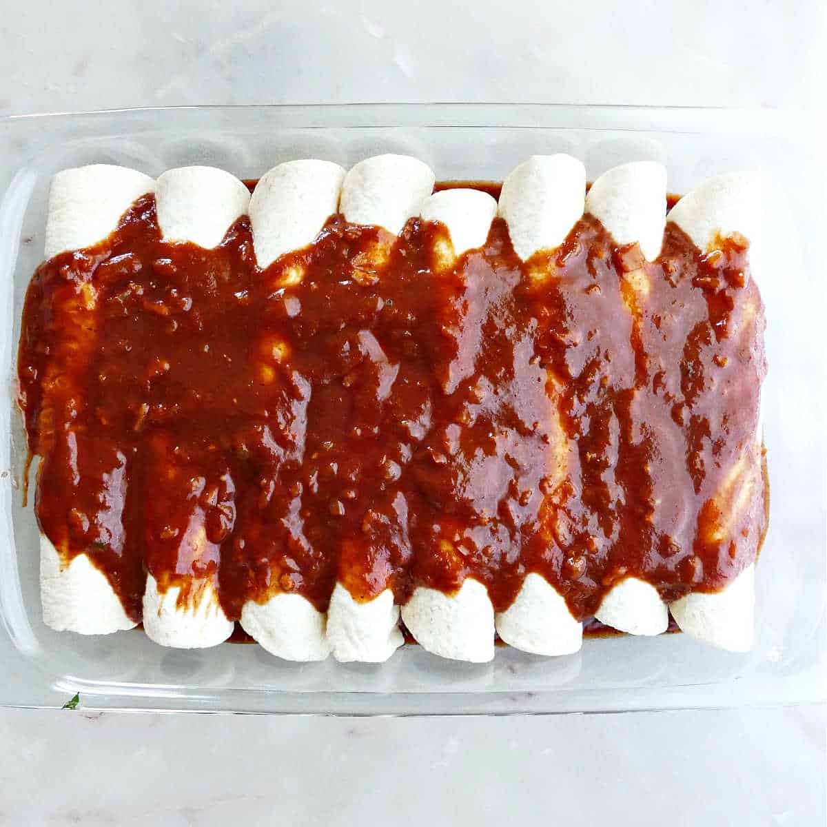enchiladas rolled up and covered with enchilada sauce in a rectangular baking dish