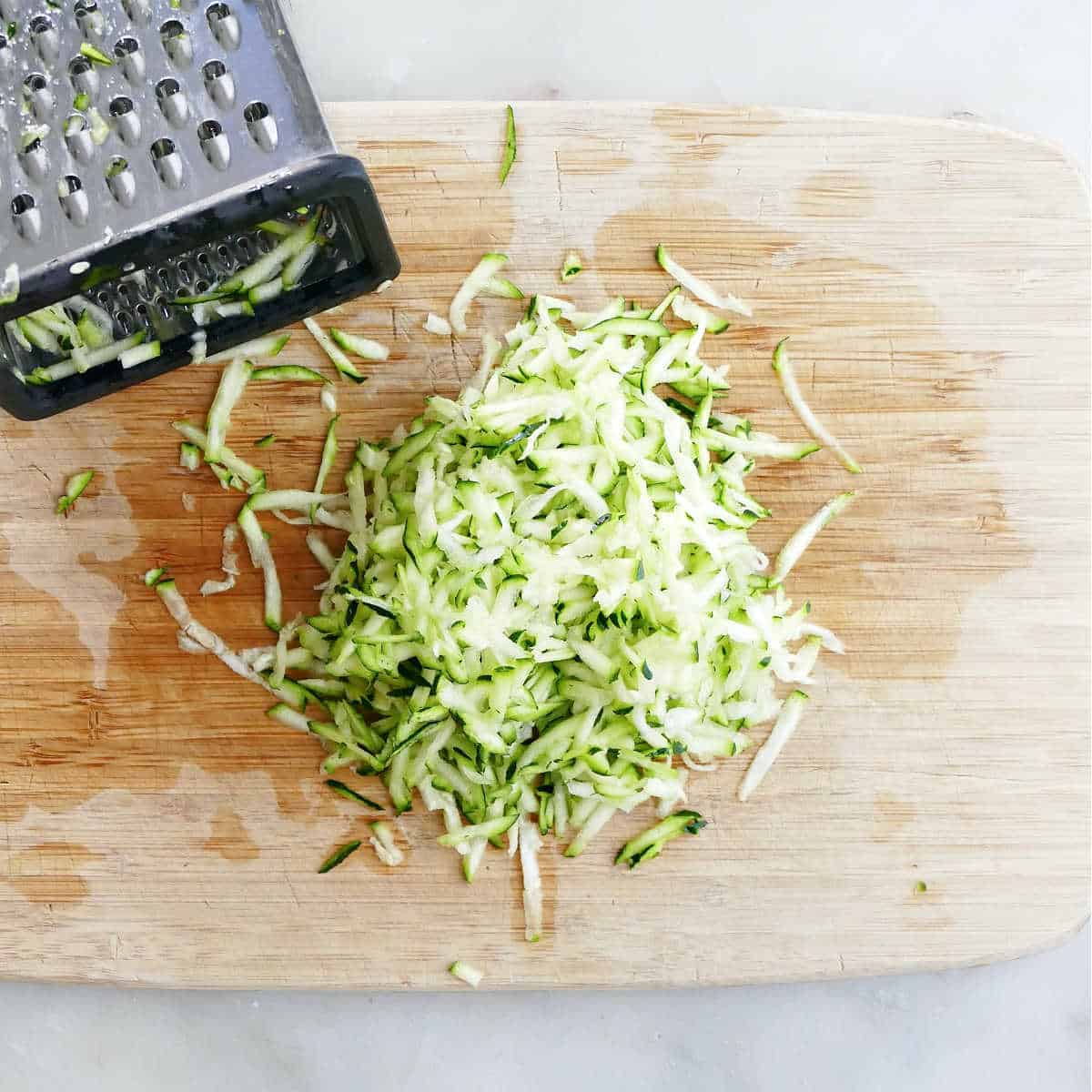 grated zucchini on a bamboo cutting board next to a box grater