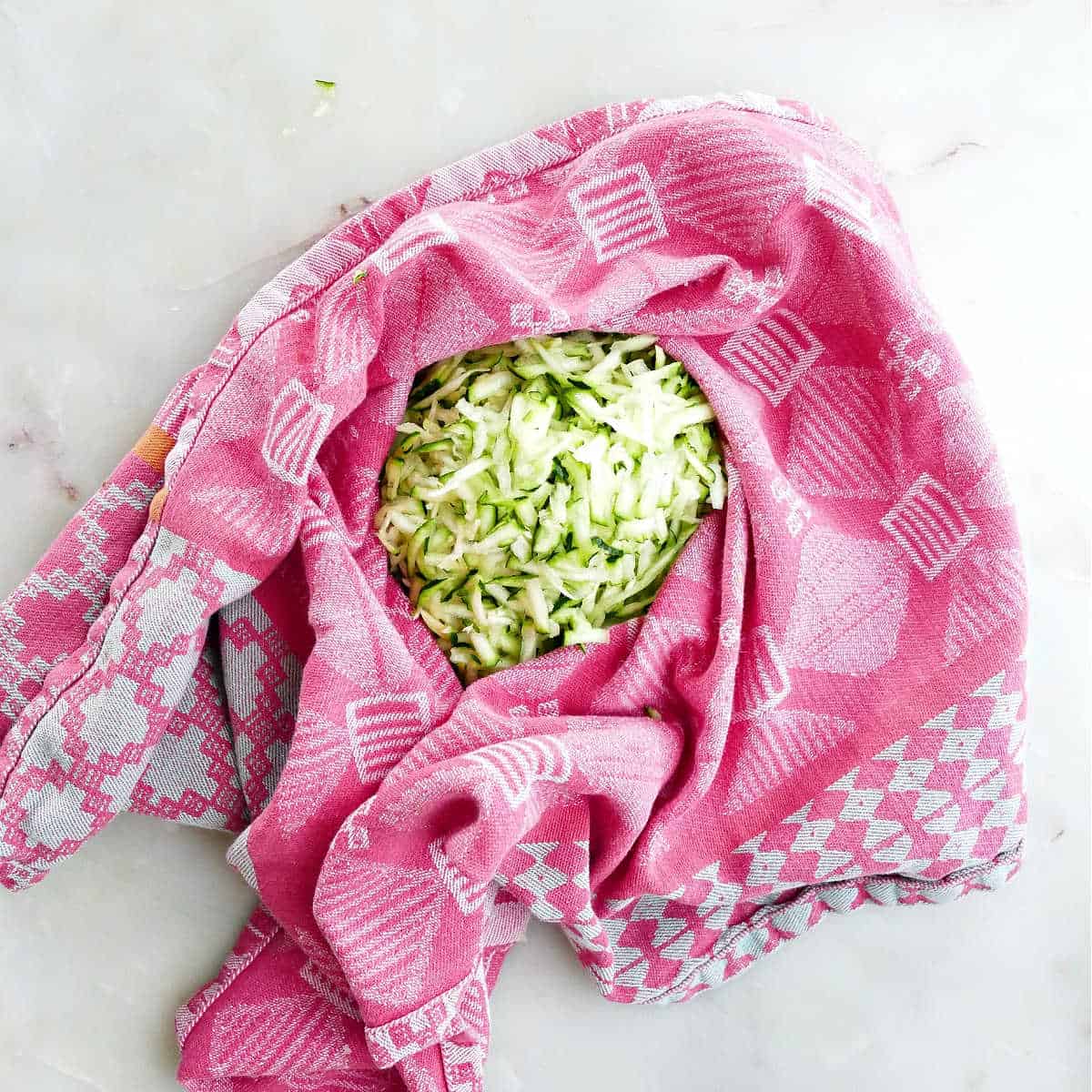 grated zucchini draining in a dish towel on a counter