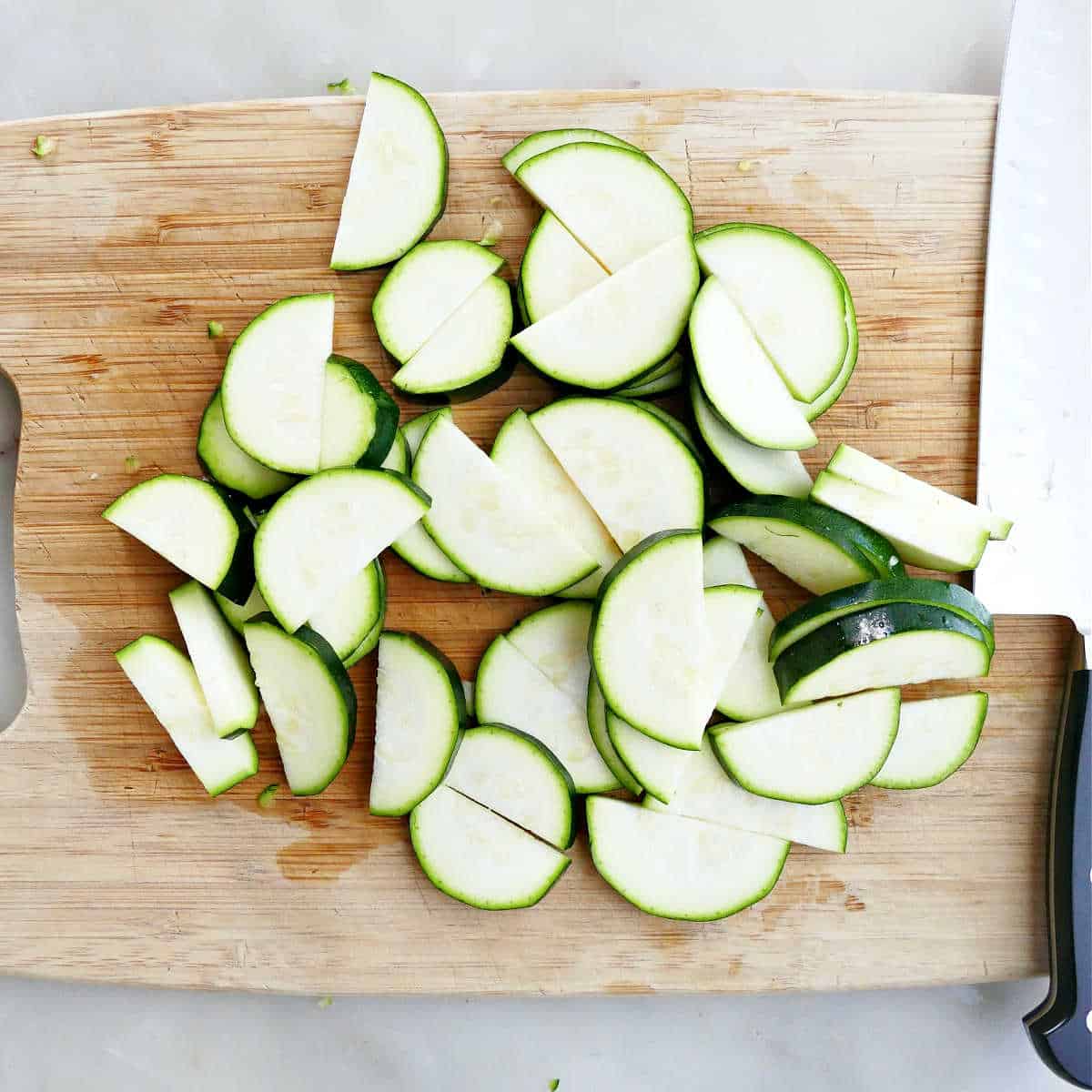 zucchini sliced into half-moons on a cutting board next to a knife