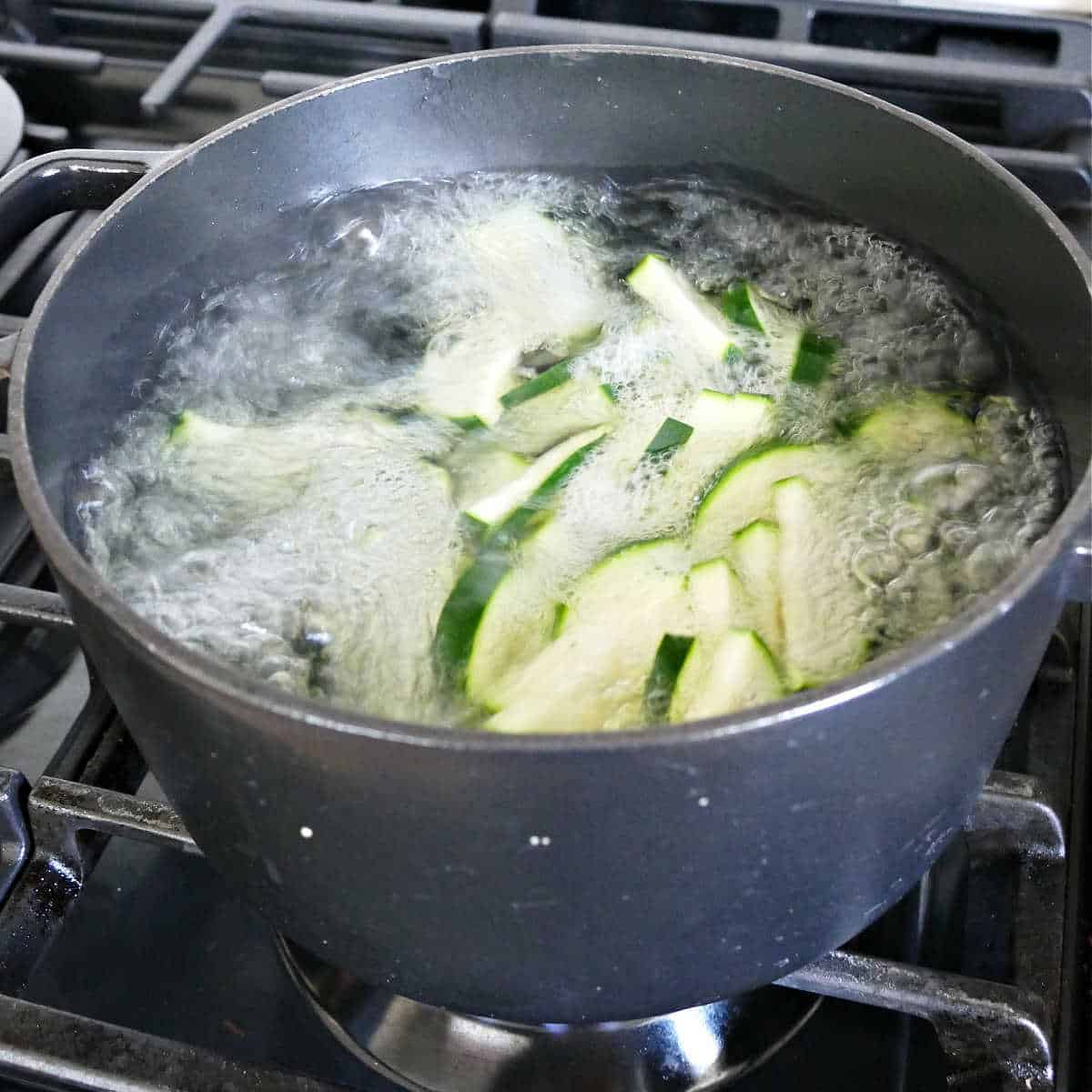 sliced zucchini being blanched in a pot of boiling water