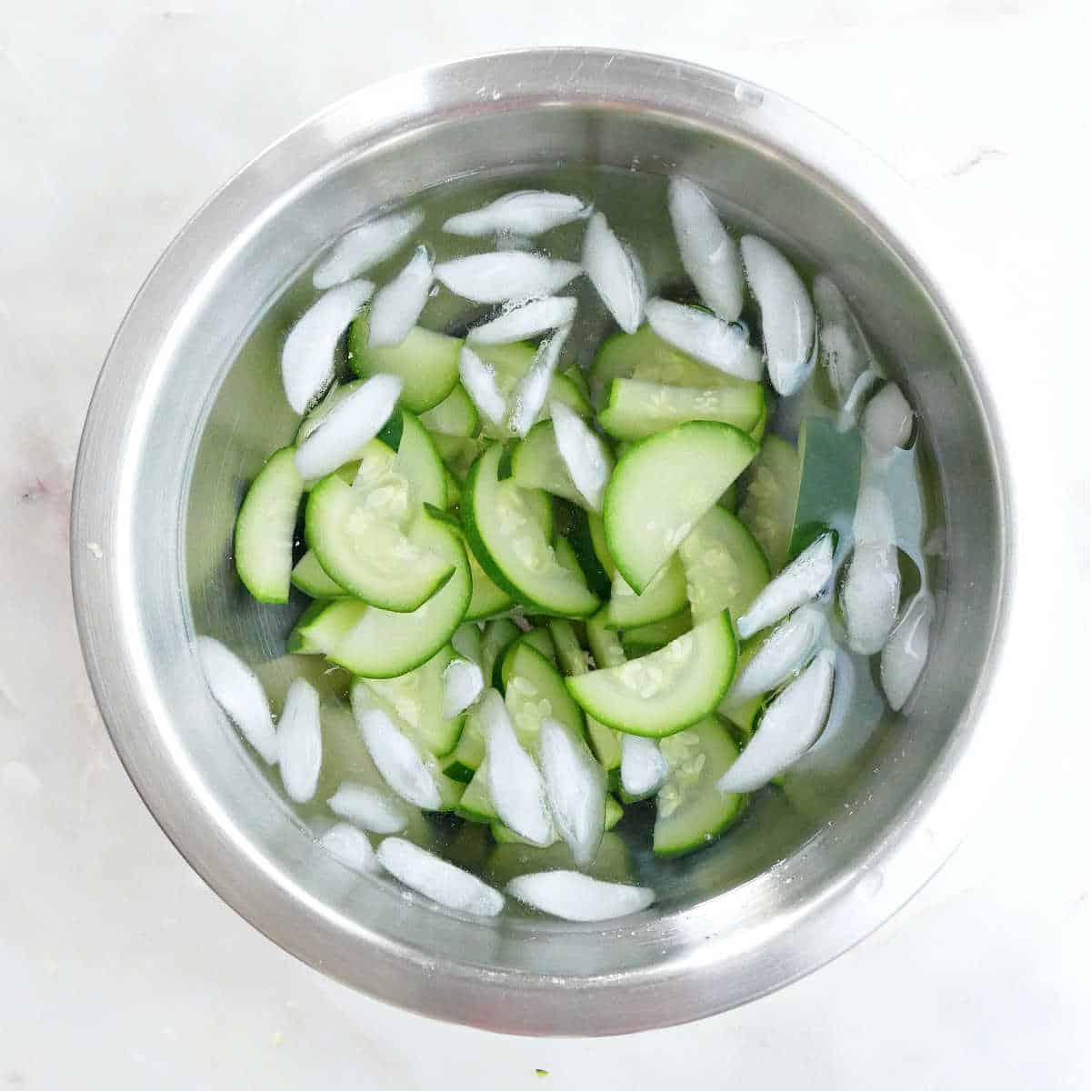 sliced zucchini in a bowl of ice water after blanching