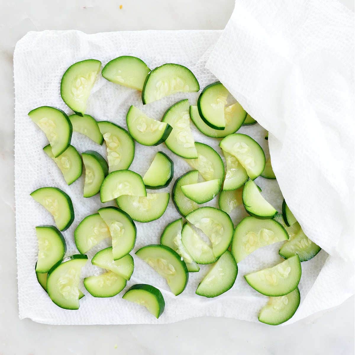 blanched zucchini slices draining on a paper towel on a counter