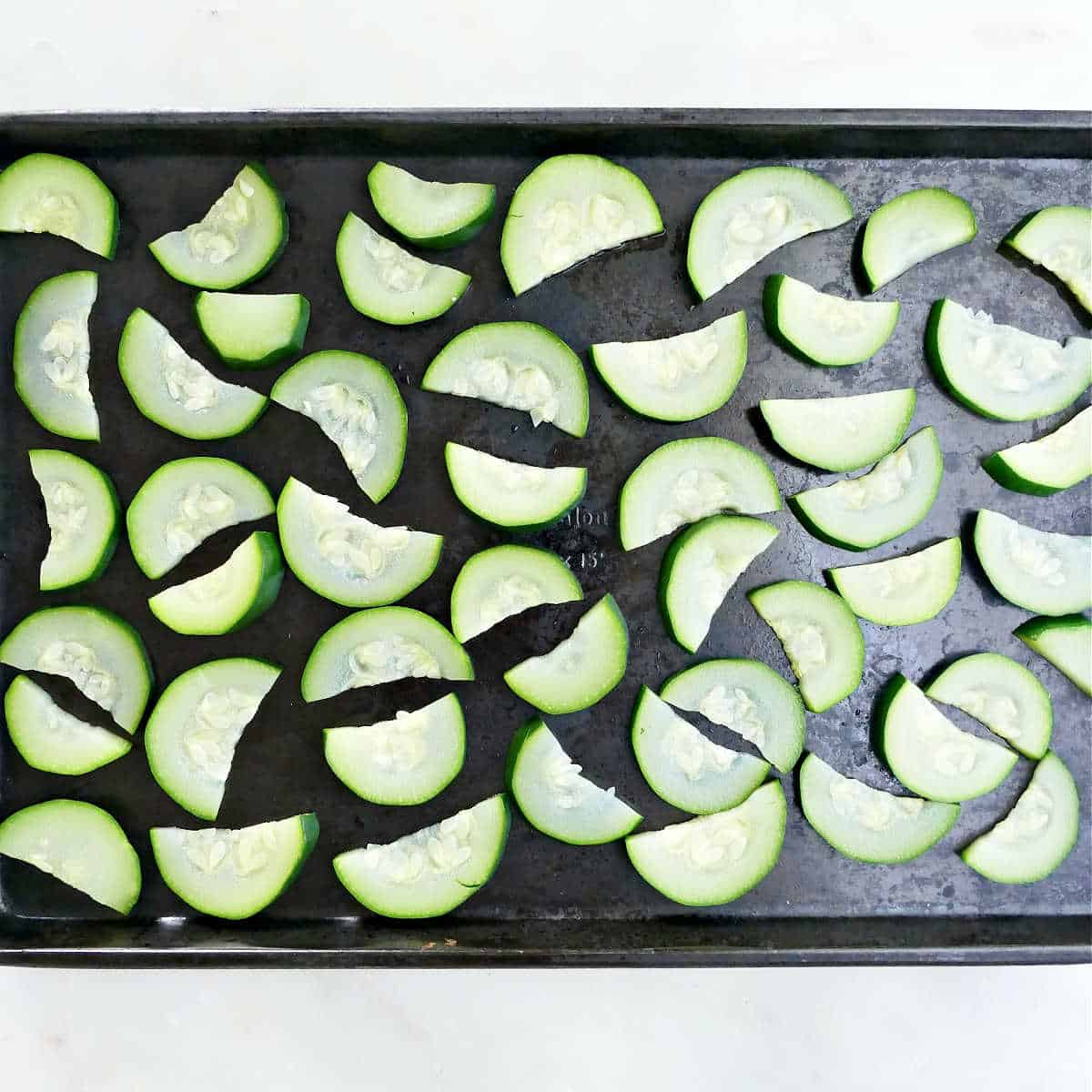 blanched zucchini slices spread out on a baking sheet before being frozen