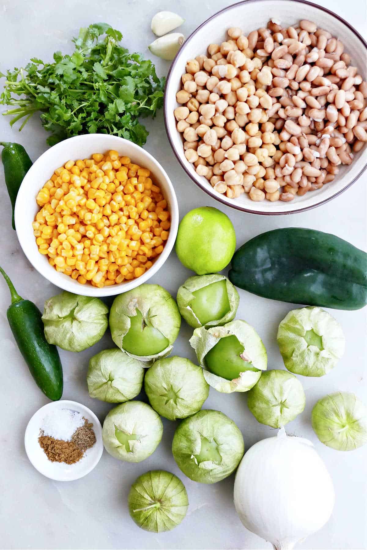 cilantro, beans, peppers, lime, tomatillos, seasonings, and corn on a counter