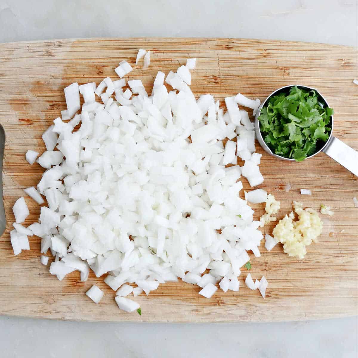 diced onion, cilantro leaves, and pressed garlic on a cutting board on a counter