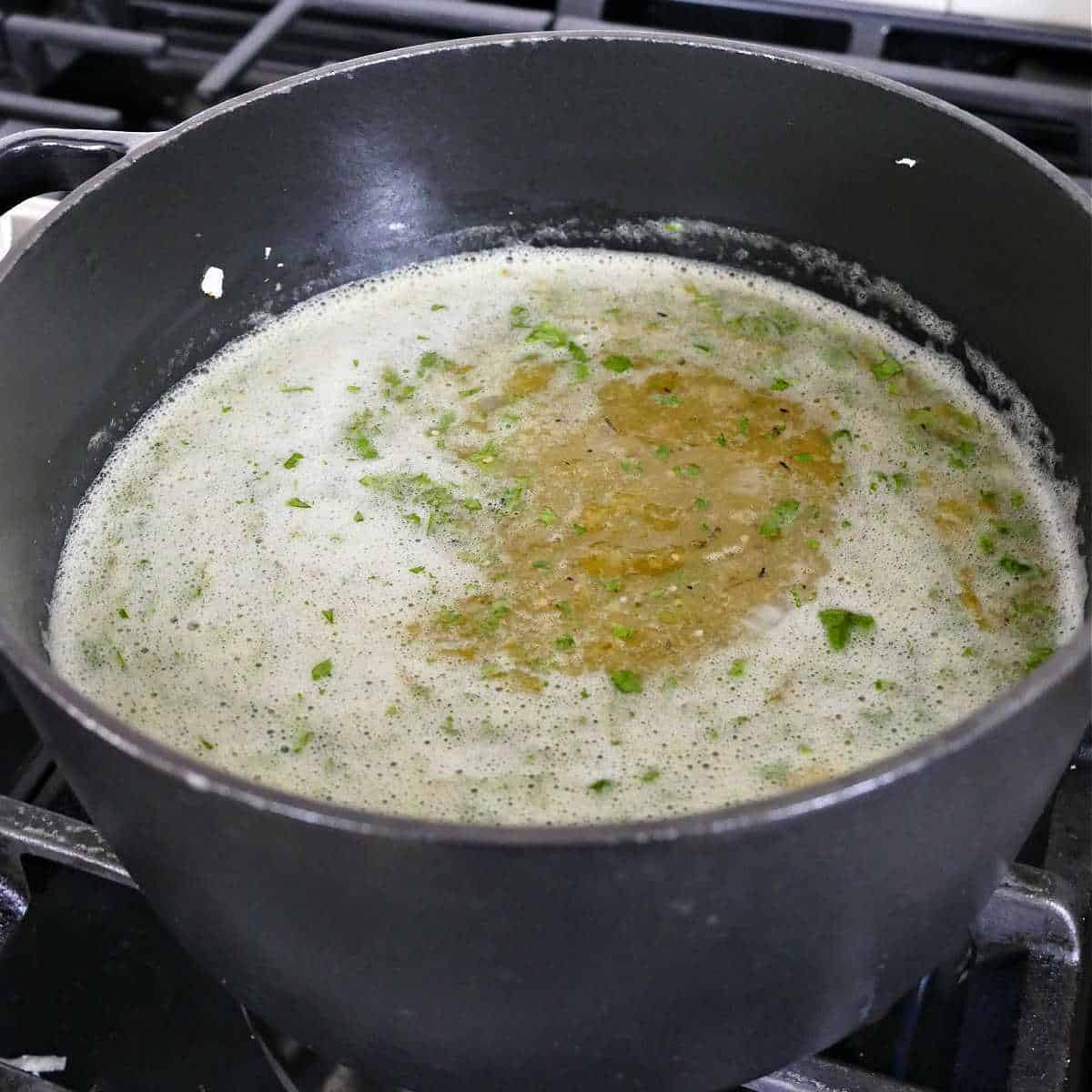 blended tomatillo and pepper mixture added to a soup pot on a stove