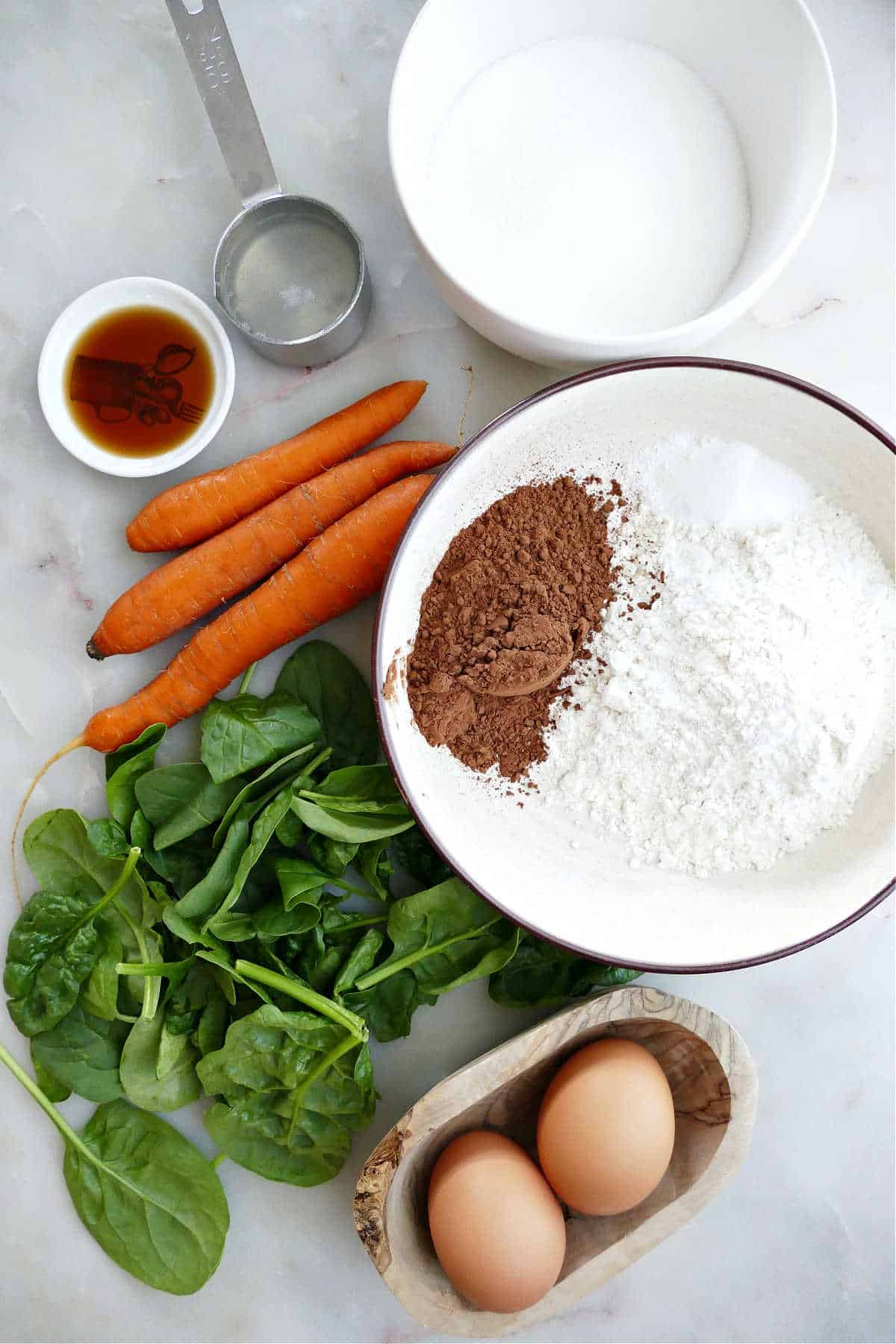 coconut oil, vanilla, sugar, flour, eggs, spinach, and carrots on a counter