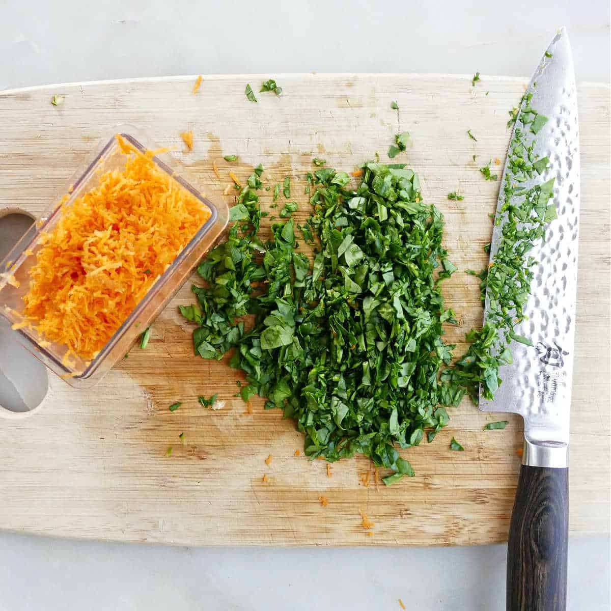 chopped spinach and shredded carrots on a cutting board on a counter