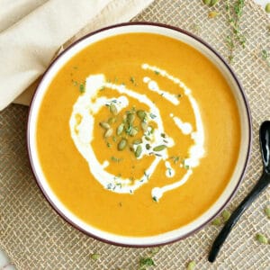carrot pumpkin soup in a bowl drizzled with cream and topped with pepitas