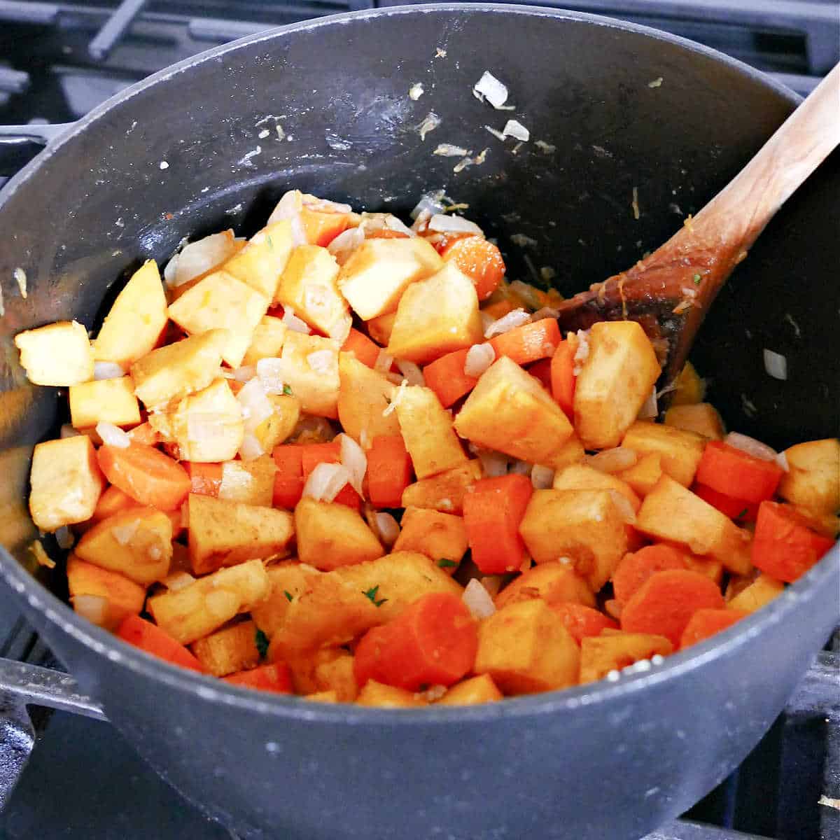 cubed carrot and pumpkin tossed in spices and cooking in a pot on a stove