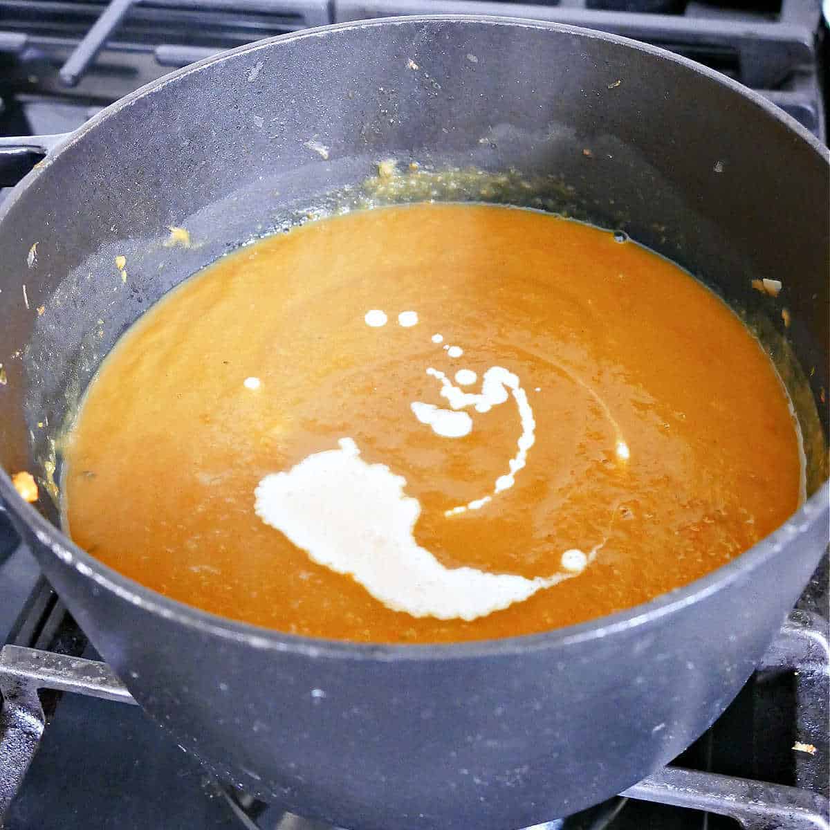 blended pumpkin and carrot soup in a pot with cream mixed into it