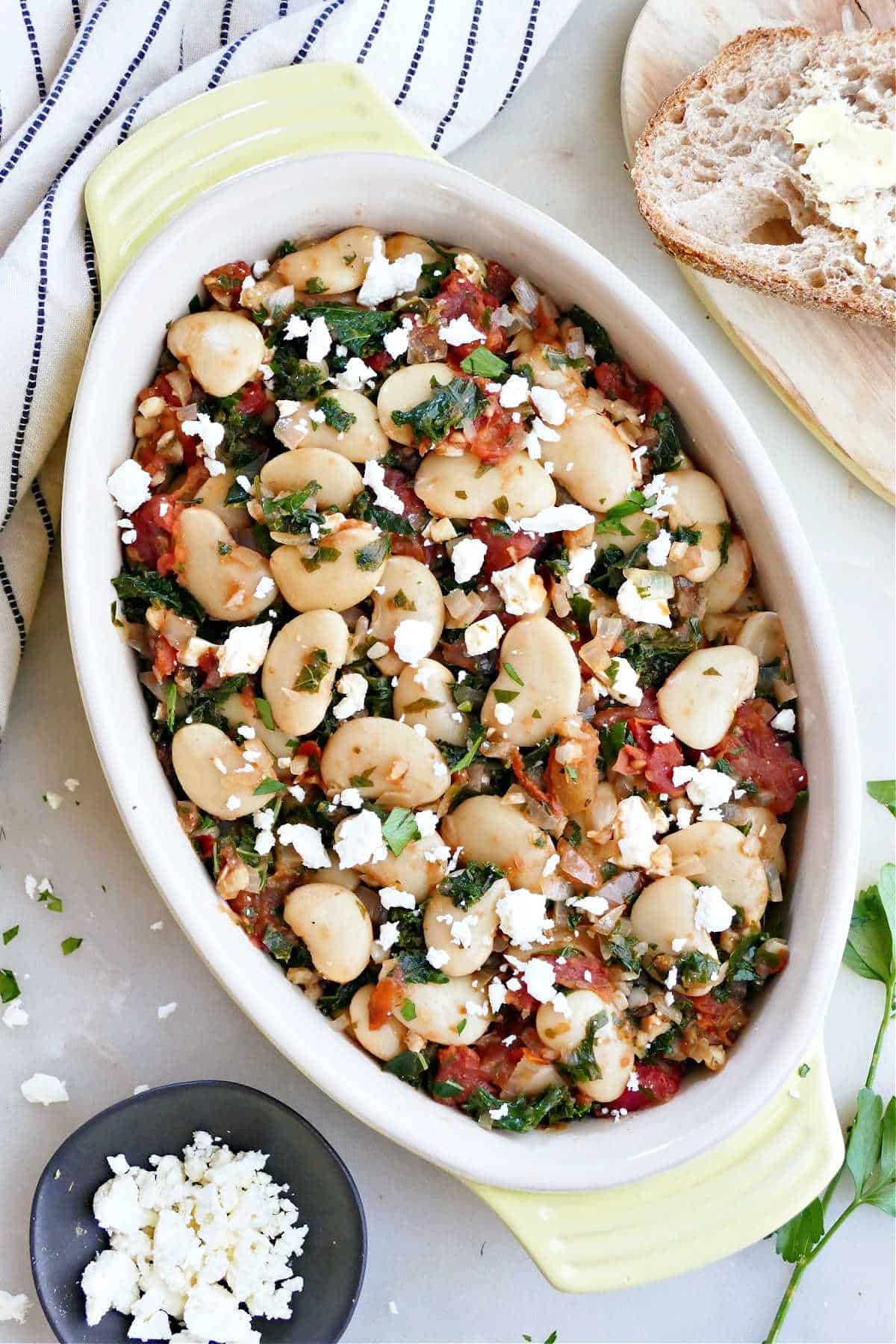 gigante beans with tomatoes, kale, and feta in an oval serving dish on a counter