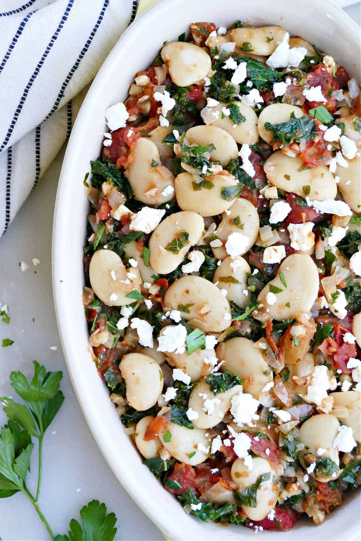 simmered gigante beans with vegetables and feta in an oval dish