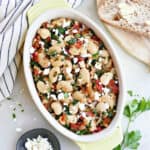 gigante beans with tomatoes, kale, and feta in an oval serving dish on a counter