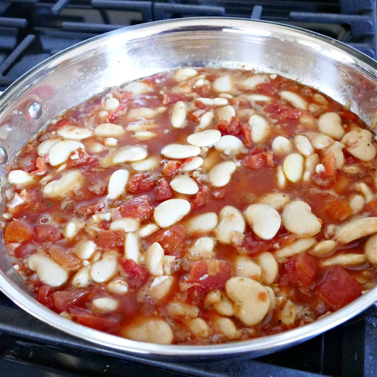 gigante beans simmering in tomatoes, shallots, garlic, and spices in a skillet
