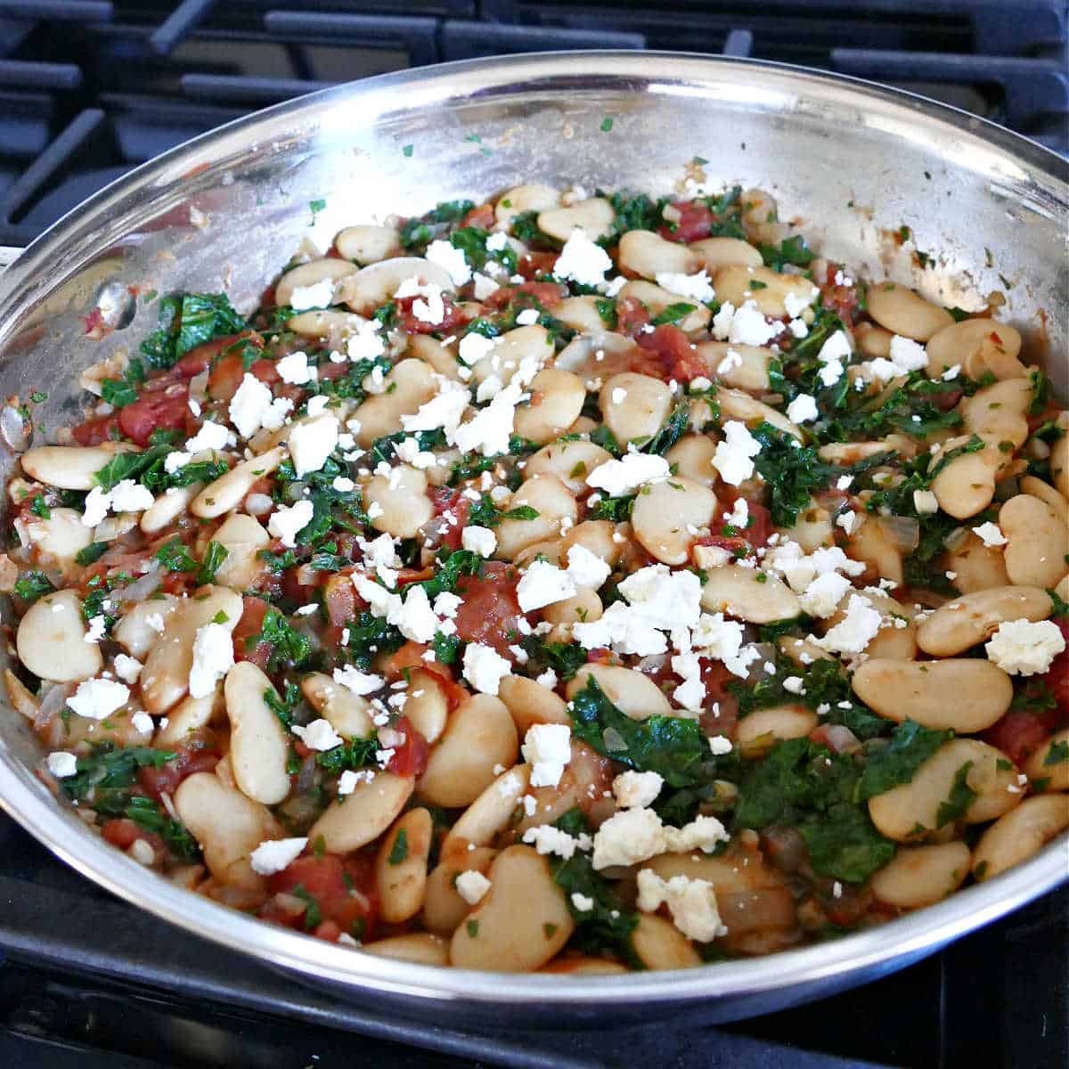 cooked gigante beans and vegetables sprinkled with feta cheese in a skillet