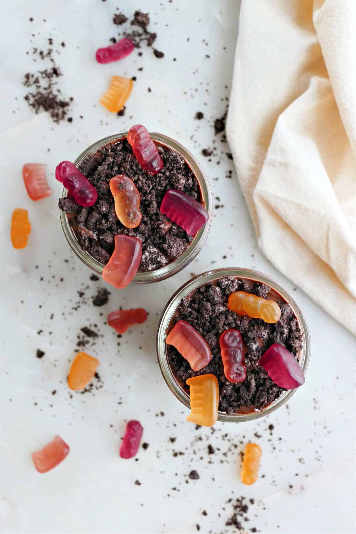two healthy dirt cups in glass jars topped with gummy candies on a counter