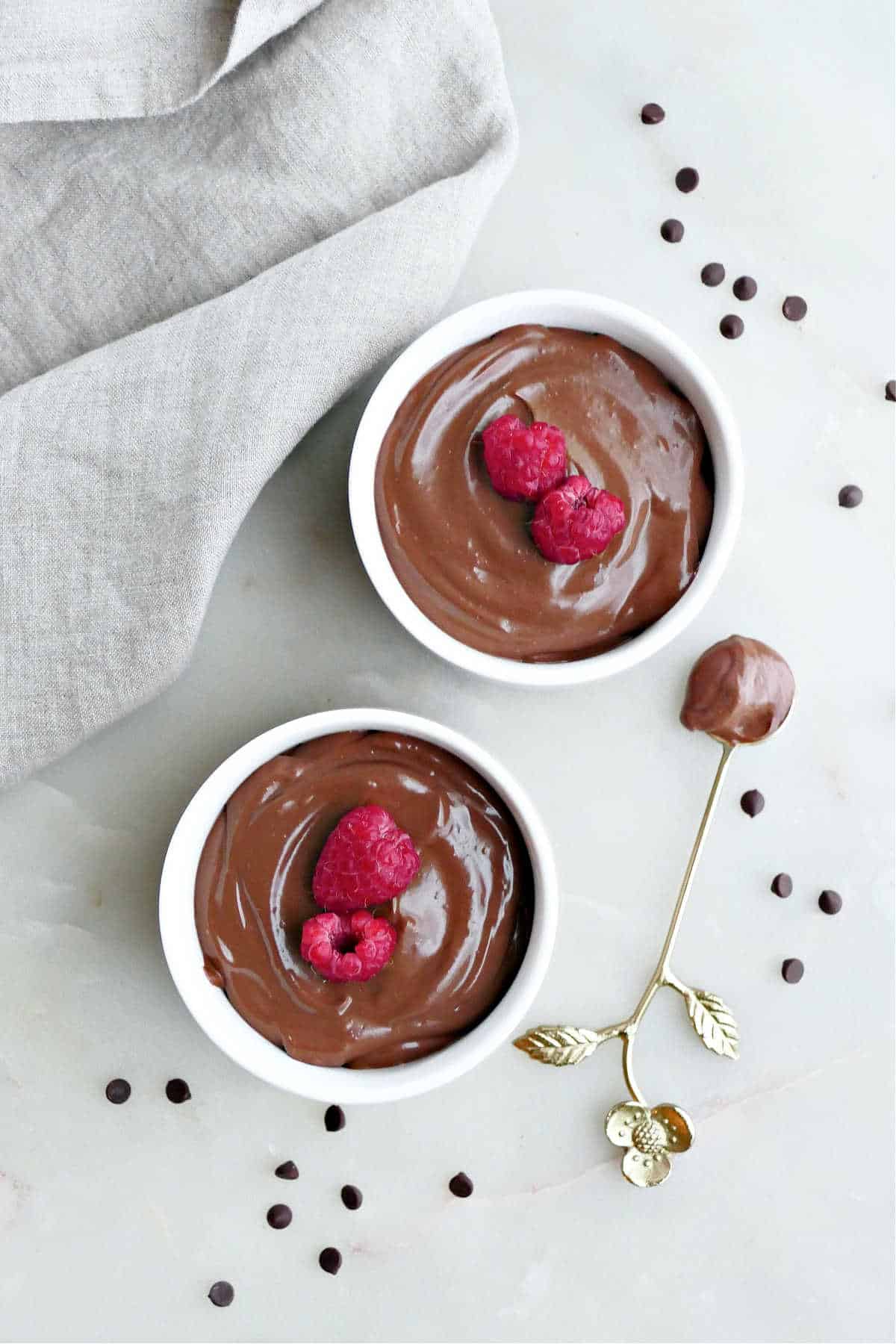 two bowls with protein chocolate mousse topped with berries next to a napkin and spoon