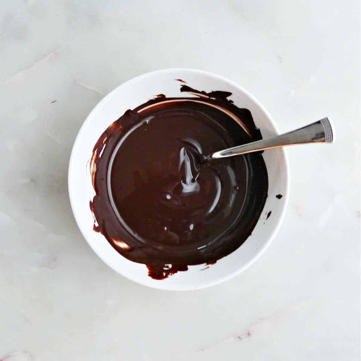 melted dark chocolate in a bowl with a spoon on a counter