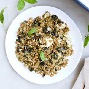 baked farro with kale on a plate next to a baking dish and napkin