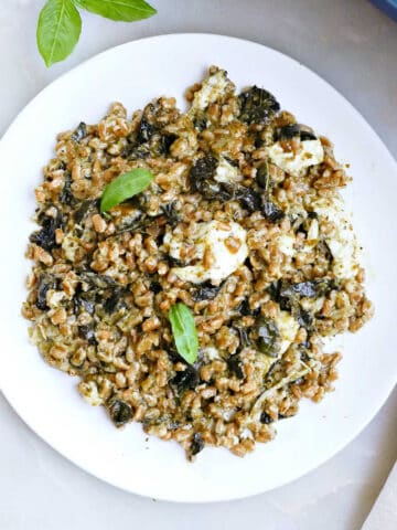 baked farro with kale on a plate next to a baking dish and napkin