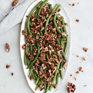 green beans topped with maple pecans on a serving dish next to napkin and spoon