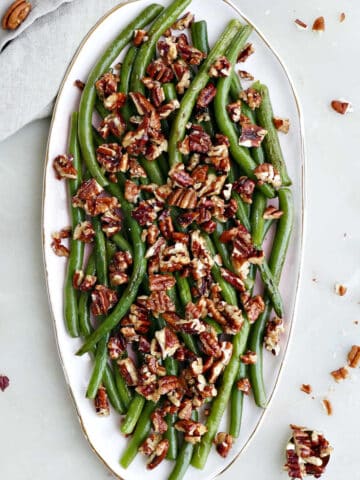 green beans topped with maple pecans on a serving dish next to napkin and spoon
