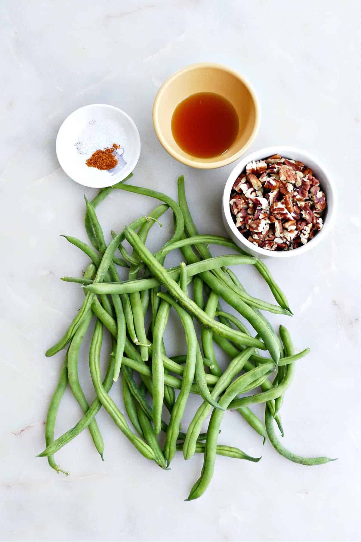 green beans, salt, cayenne pepper, maple syrup, and chopped pecans on a counter