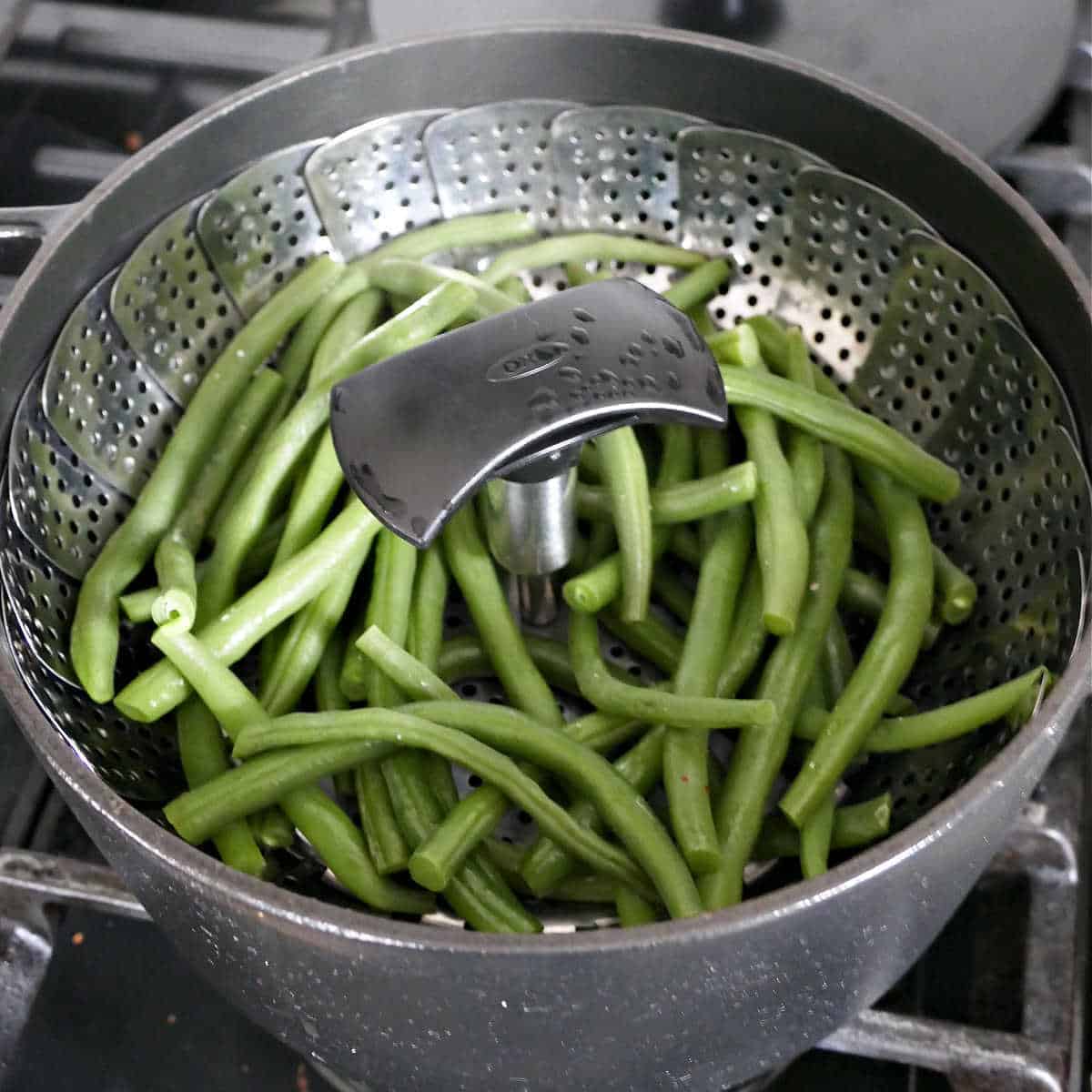 steamed green beans in a vegetable basket in a pot on a stove
