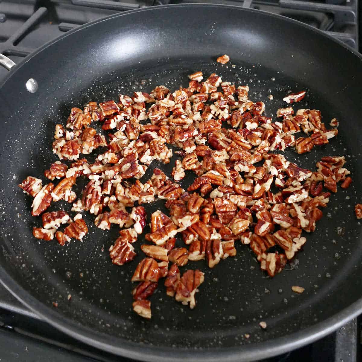 candied maple pecans cooking in a skillet on a stove