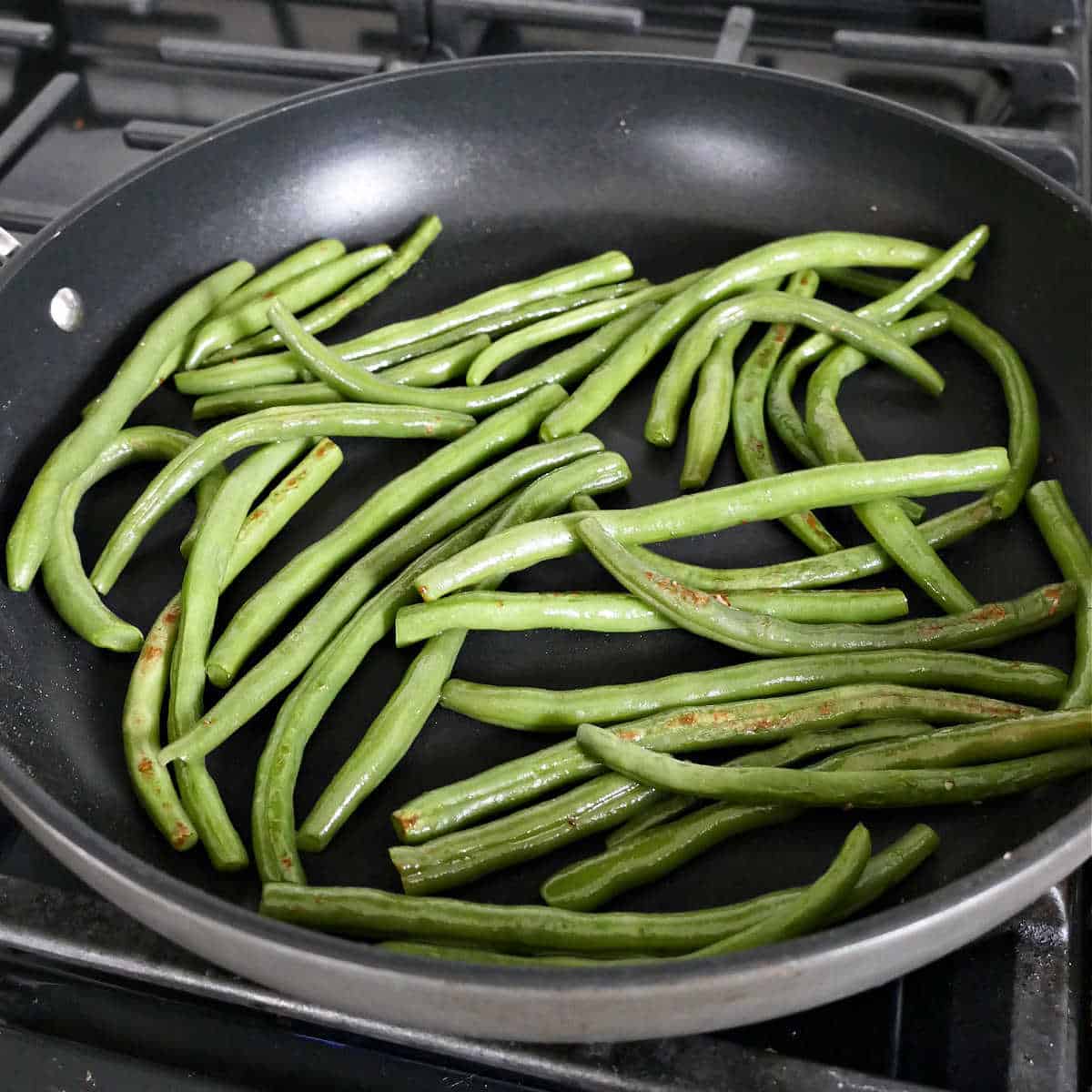 steamed green beans being sautéed in a skillet on a stove