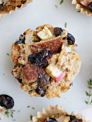 stuffing muffin with dried cranberries surrounded by more muffins on a counter