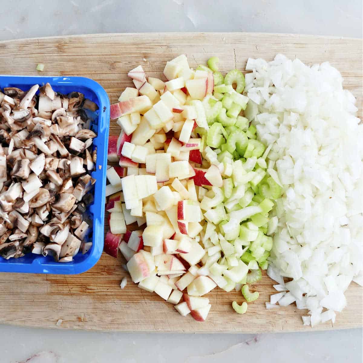diced mushrooms, apples, celery, and onion next to each other on a cutting board