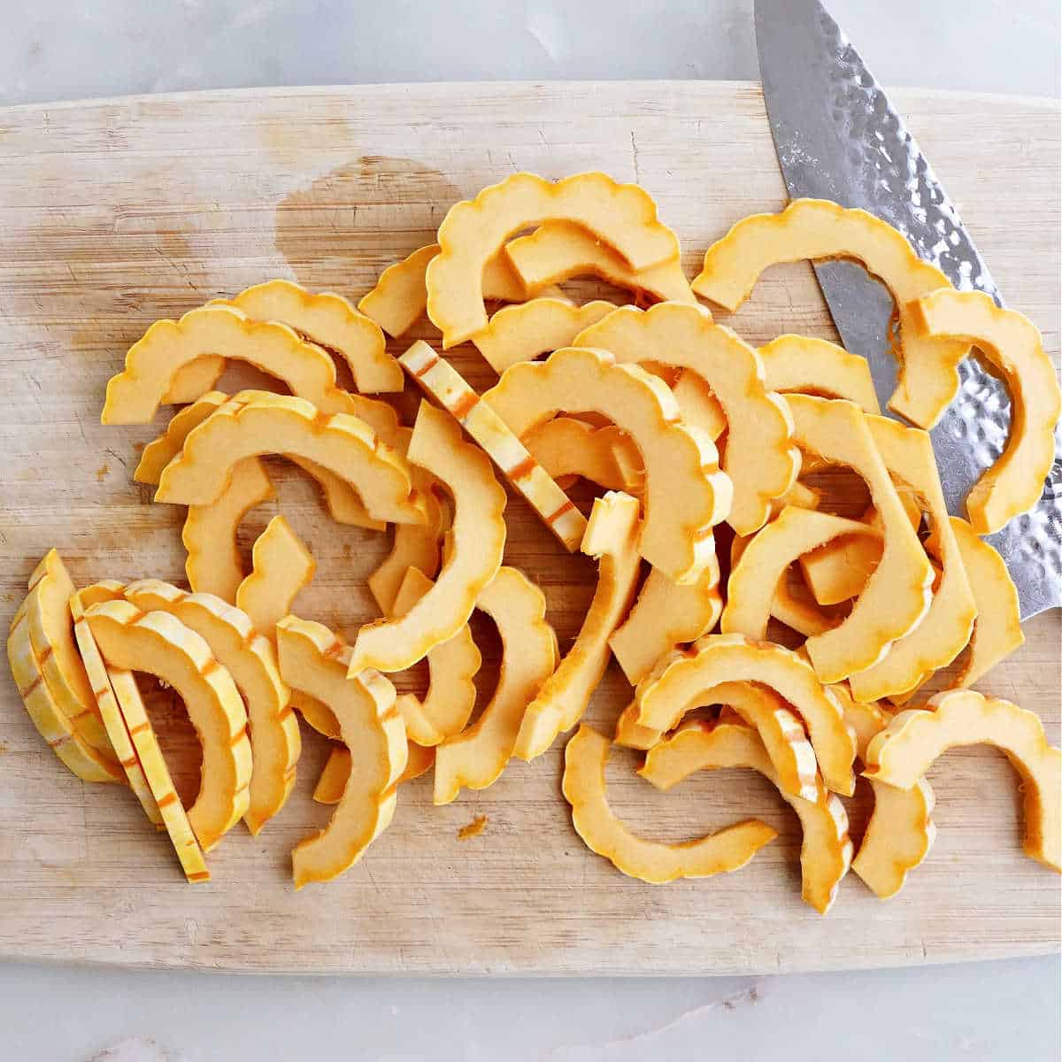 delicata squash sliced into half-moon pieces on a cutting board with a knife