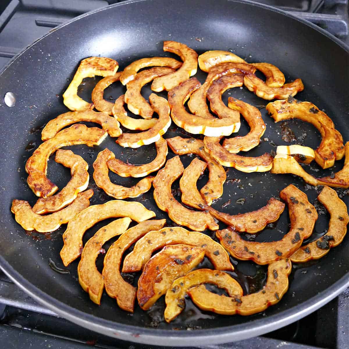pan fried delicata squash pieces in a skillet on a stove