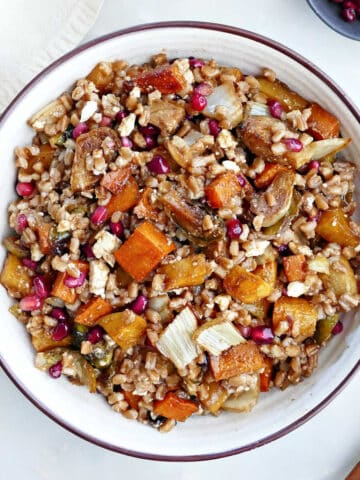 winter farro salad in a serving bowl next to spoon, napkin, and pomegranates