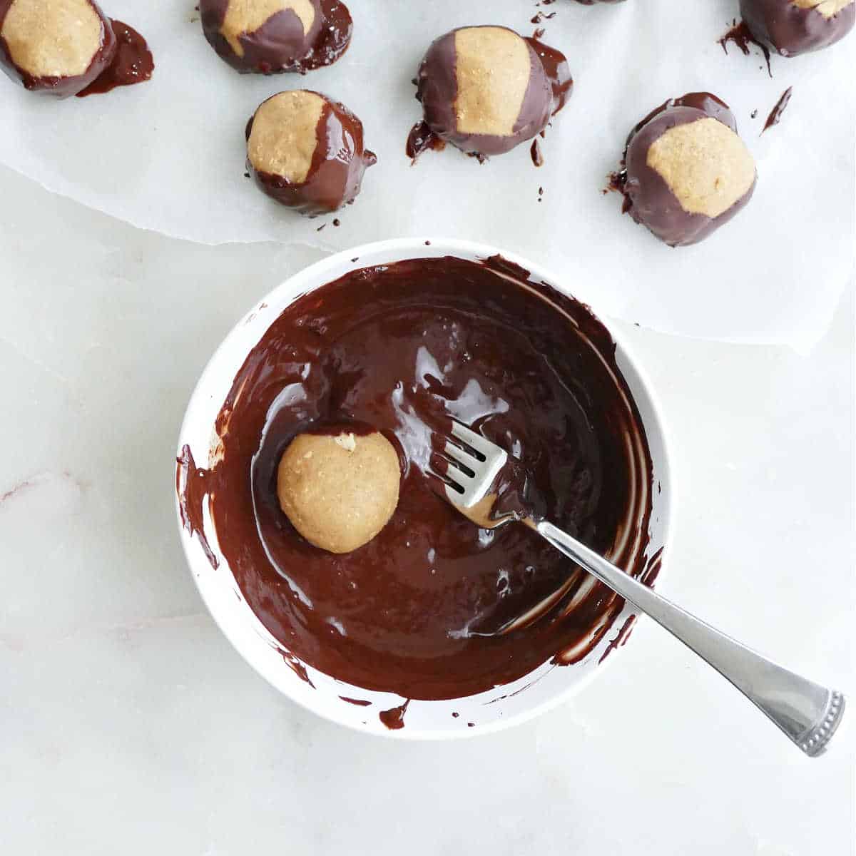 buckeye ball being dipped in a bowl of melted chocolate with a fork